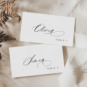 May include: Two white place cards with black calligraphy. The top card reads "Olivia Table 1" and the bottom card reads "Simon Table 3".