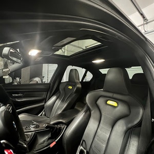 May include: Black leather interior of a car with a sunroof. The car has two black leather bucket seats with yellow accents. The seats have a sporty design with a high back and side bolsters.