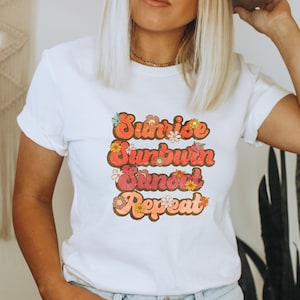 Könnte beinhalten: Weißes T-Shirt mit einer Retro-Grafik, auf der "Sunrise Sunburn Sunset Repeat" in Orange, Rosa und Braun mit floralen Akzenten steht.