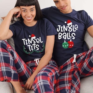 K&ouml;nnte beinhalten: Passende marineblaue Weihnachts-Pyjama-Sets. Jedes Set enth&auml;lt ein marineblaues T-Shirt mit Weihnachtsm&uuml;tze und einem humorvollen Spruch, kombiniert mit rot-wei&szlig;-blau karierten Pyjamahosen. Die Sets sind f&uuml;r Paare oder Freunde konzipiert.