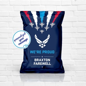 Puede incluir: Bolsa de regalo azul marino con un diseño que presenta aviones de combate y el texto "WE'RE PROUD". La bolsa incluye el emblema de la Fuerza Aérea y espacio para un mensaje personalizado. El diseño de la bolsa incluye detalles en rojo, blanco y azul.