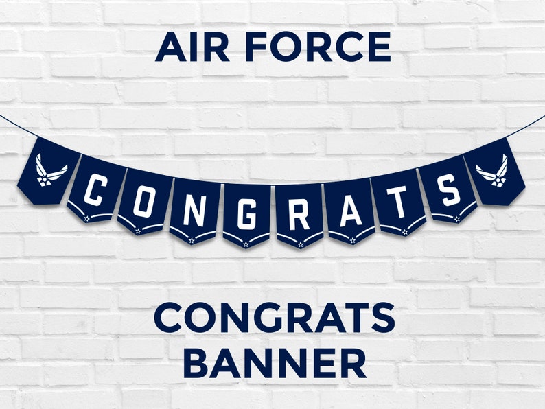 May include: Blue and white banner with the text "CONGRATS" and the Air Force logo on each end. The banner is hanging on a white brick wall. The text "CONGRATS BANNER" is below the banner.