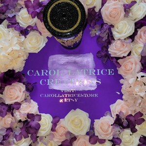 May include: A black and gold candle holder with rhinestones sits on a purple background surrounded by white and pink roses and purple flowers. The text "CAROL LATRICE CREATIONS VISIT CAROLLATRICESTORE @ETSY" is printed on the background.