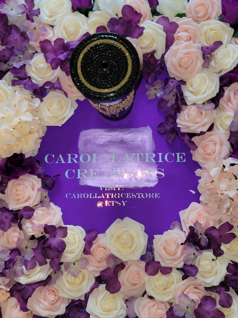 May include: A black and gold candle holder with rhinestones sits on a purple background surrounded by white and pink roses and purple flowers. The text "CAROL LATRICE CREATIONS VISIT CAROLLATRICESTORE @ETSY" is printed on the background.