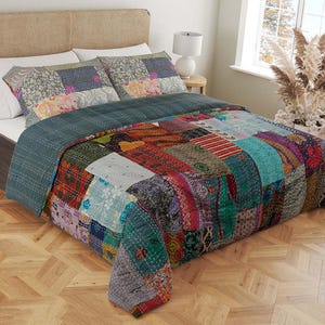 Può includere: Un piumone patchwork colorato con uno sfondo blu-verde. Il piumone è fatto di vari tessuti in tonalità di rosso, arancione, giallo, verde, blu e viola. Il piumone è su un letto con una testiera in legno.