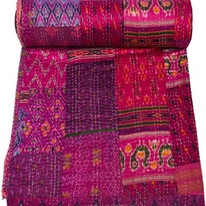 May include: A pink and purple kantha quilt with a patchwork design. The quilt is made of recycled saris and is hand-stitched. It is a traditional Indian textile.