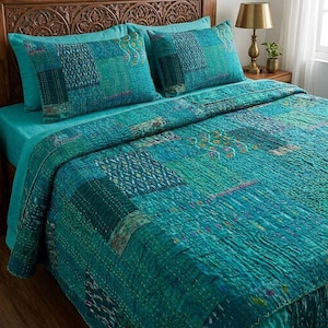 May include: A teal patchwork quilt and two matching pillowcases on a bed with a teal sheet. The quilt features teal and green fabric squares stitched together. The headboard is carved wood, and a lamp sits on the bedside table.