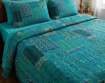 May include: A teal patchwork quilt and two matching pillowcases rest on a bed with a teal sheet. The quilt features a variety of teal and green fabric squares stitched together. The headboard is made of carved wood, and a lamp sits on the nightstand.