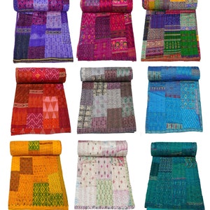 May include: Nine kantha quilts in various colors and patterns, including purple, pink, red, orange, blue, green, and white. The quilts are made of recycled saris and are hand-stitched. They are rolled up and displayed on a white background.