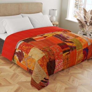 Peut inclure: Une courtepointe patchwork dans des tons de rouge, orange et marron. La courtepointe est faite de différents tissus et a un aspect unique et fait main.