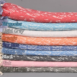 Könnte beinhalten: Ein Stapel von zehn türkischen Handtüchern in verschiedenen Farben, darunter Rot, Türkis, Hellgrau, Orange, Blau, Petrolblau, Schwarz, Rosa und Khaki. Die Handtücher haben ein weißes Spritzmuster.