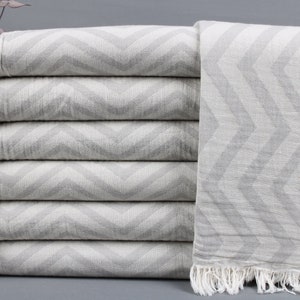 May include: A stack of six gray and white chevron patterned towels with white fringe. The towels are folded neatly, showcasing the zigzag design. The towels are made of a soft, textured material.