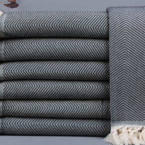 May include: A stack of six folded gray and white chevron patterned towels. The towels have a fringe on the edges. The towels are made of a soft material and are suitable for use in a bathroom or spa.