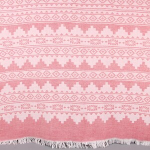 Pode incluir: Um t&ecirc;xtil cor-de-rosa com um padr&atilde;o geom&eacute;trico. O design apresenta filas de formas repetidas em branco, incluindo tri&acirc;ngulos e figuras em forma de diamante. A borda inferior tem uma franja.
