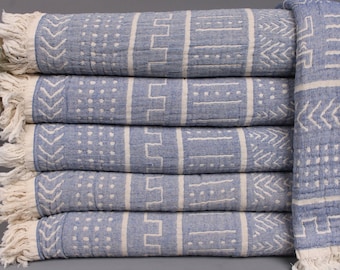 May include: A stack of six blue and white patterned towels with fringe edges. The towels have a geometric design and are made of cotton.