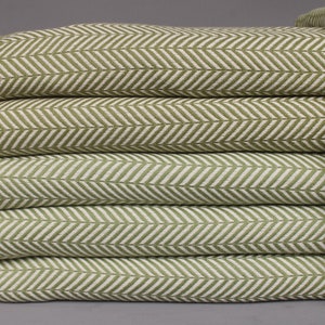 May include: A stack of six green and white herringbone-patterned towels. The towels have a soft, textured appearance with a fringe detail on the ends. The color palette is a mix of light green and white.
