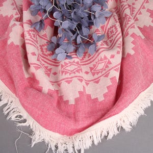 Pode incluir: Uma toalha de praia redonda com estampa rosa e branca com borda com franjas. A toalha apresenta um design geom&eacute;trico e &eacute; adornada com raminhos decorativos azuis.