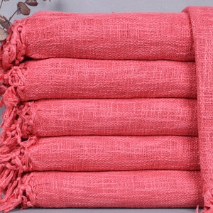 May include: A stack of six coral-colored woven throws with fringed edges. The throws are neatly folded, showcasing a textured weave. The color is a vibrant, warm hue, suitable for home decor.