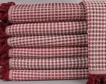 May include: A stack of six red and white patterned towels with fringed edges. The towels have a geometric diamond pattern and are folded neatly. The fringe is a darker shade of red. The towels are likely made of a soft, absorbent material.