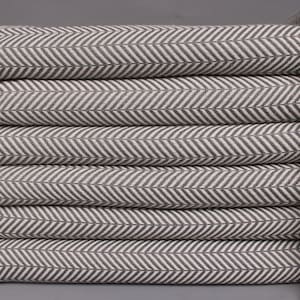 May include: A stack of six gray and white herringbone patterned towels with white fringe.