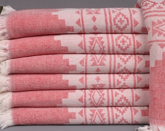 Puede incluir: Una pila de seis toallas estampadas en rojo y blanco con bordes con flecos. Las toallas presentan un diseño geométrico en blanco sobre un fondo rojo. Las toallas están dobladas y apiladas cuidadosamente, mostrando el intrincado patrón.