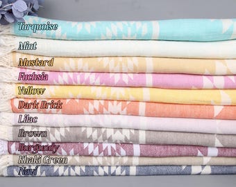 May include: A stack of colorful Turkish towels in various shades, including turquoise, mint, mustard, fuchsia, yellow, dark brick, lilac, brown, burgundy, khaki green, and navy. Each towel features a geometric pattern and fringed edges.