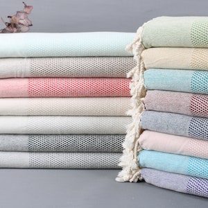 Può includere: Una pila di dieci asciugamani turchi in vari colori, tra cui azzurro, rosa, beige, grigio e verde. Gli asciugamani sono in cotone e hanno una trama a nido d'ape.