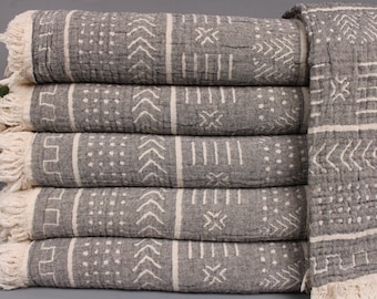 May include: A stack of gray and white patterned towels. The towels have a geometric design with white lines and shapes on a gray background. The edges of the towels have a fringed trim. The towels are folded and stacked neatly.