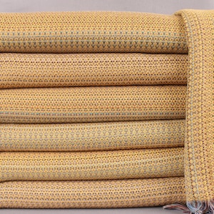May include: A stack of six yellow woven blankets with a geometric pattern. The blankets have a fringe on the edges.