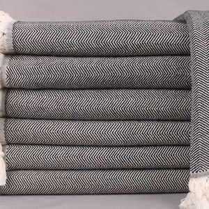 Puede incluir: Una pila de toallas de color blanco y negro con un patrón de espiga y flecos blancos.