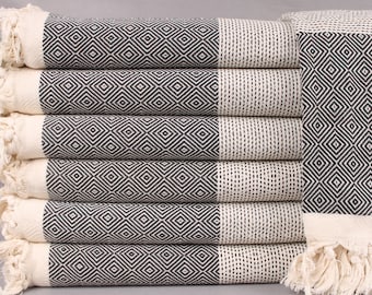 May include: A pile of six black and white diamond-patterned towels with fringed edges. The towels are folded and stacked, displaying the geometric design. The colour scheme is neutral, with a mix of black and cream.