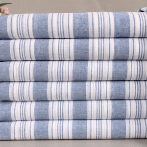 May include: A stack of six blue and white striped towels with white fringe. The towels are folded neatly, showcasing the alternating stripes. The towels are made of a textured fabric.