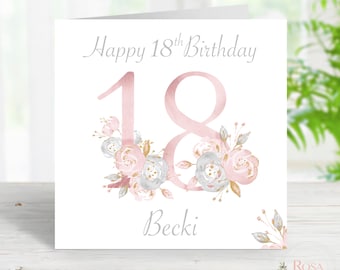 May include: A white greeting card with the text "Happy 18th Birthday" in gray script. The number "18" is in pink, adorned with floral arrangements in pink, gray, and gold. The name "Becki" is written below the number.