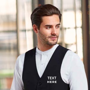 Puede incluir: Un chaleco negro con un texto bordado en blanco que dice "TEXT HERE" en la parte delantera. CHALECO PERSONALIZADO CON BORDADO.