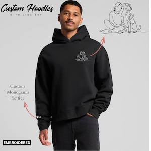 以下が含まれることがあります： 人、犬の線画デザインが施された黒いパーカー。「Custom Hoodies with Line Art」の文字が上部に、「Custom Monograms for free」の文字が側面にあります。「EMBROIDERED」の文字が下部にあります。