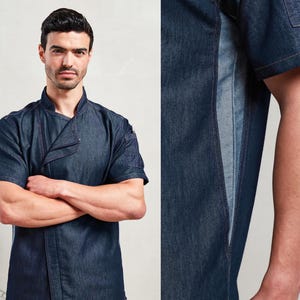 May include: A dark blue denim chef's jacket with short sleeves and a mandarin collar. The jacket features a contrasting lighter blue panel down the side and a small pocket on the sleeve. The model has their arms crossed.