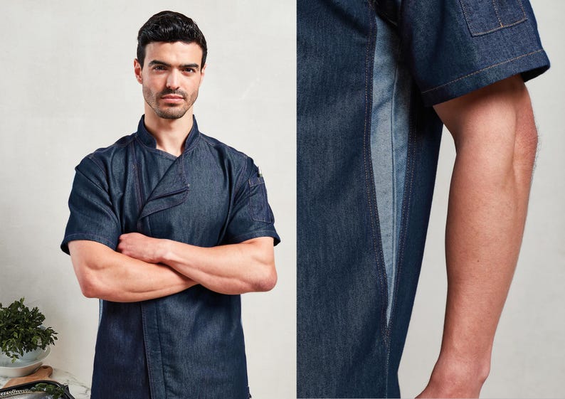 May include: A dark blue denim chef's jacket with short sleeves and a mandarin collar. The jacket features a contrasting lighter blue panel down the side and a small pocket on the sleeve. The model has their arms crossed.
