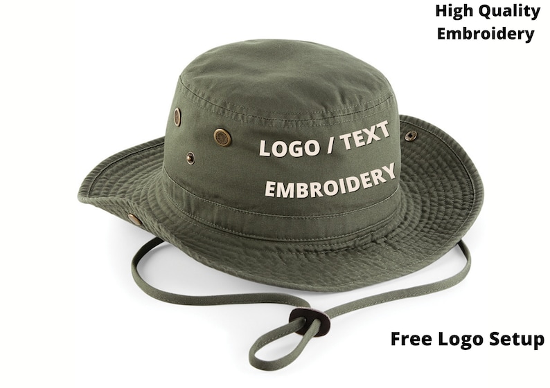 Puede incluir: Sombrero de pescador verde oliva con ala ancha y correa de barbilla ajustable. Cuenta con ojales met&aacute;licos y el texto "LOGO / TEXT EMBROIDERY" en blanco. El sombrero est&aacute; dise&ntilde;ado para bordado personalizado.
