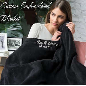 Puede incluir: Una manta de forro polar negra con bordado blanco que dice "Roy & Emily 6th April 2025".