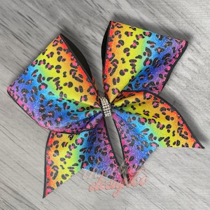 May include: A large rainbow cheetah print cheer bow with a black base and a silver rhinestone in the center.