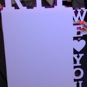 May include: A white wooden sign with the letters "RIP" at the top and "WE LOVE YOU" vertically along the side. The letters have a purple and pink patterned border. The sign has a blank white space for a photo.