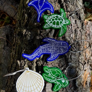 May include: A collection of ocean-themed keychains featuring a blue manta ray, green sea turtles, a blue whale shark, and a white seashell with gold accents. Each keychain is attached to a silver metal loop.
