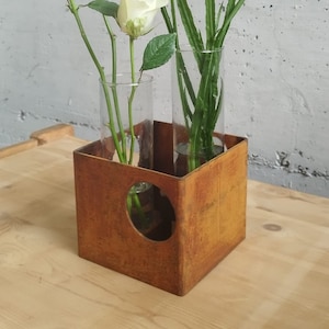 以下が含まれることがあります： さびた金属製のフラワーベースに、白いバラと紫の花を挿したガラスの筒が2本入っています。ベースにはハート型の切り抜きがあります。