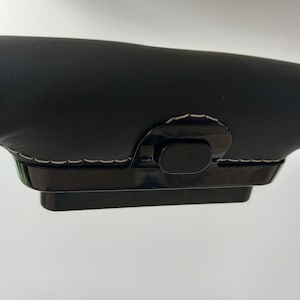 Op de afbeelding: Zwarte lederen stuurwielhoes met een zwarte plastic knop en witte stiksels.