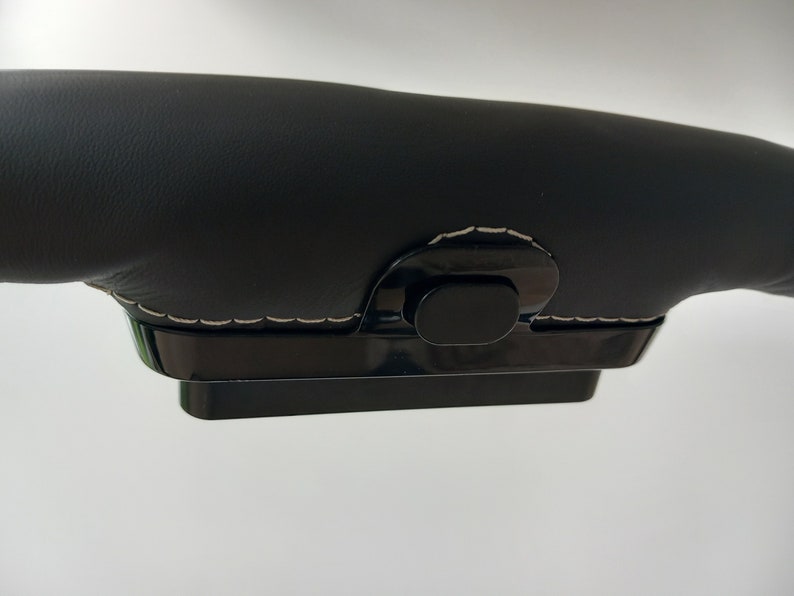 Op de afbeelding: Zwarte lederen stuurwielhoes met een zwarte plastic knop en witte stiksels.