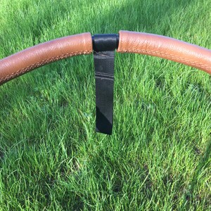 May include: A black stroller handlebar with brown leather grips and a black strap.