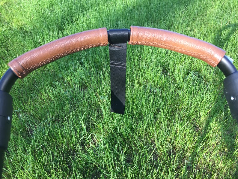 May include: A black stroller handlebar with brown leather grips and a black strap.