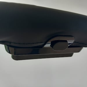 May include: A black leather armrest with a black plastic release button.