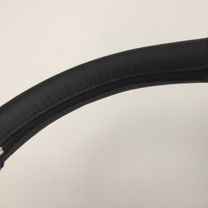 May include: Black leather handlebar cover with a zipper. The cover is designed to fit over a stroller handlebar.