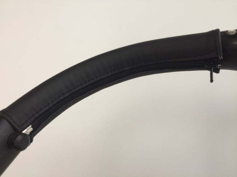 May include: Black leather handlebar cover with a zipper. The cover is designed to fit over a stroller handlebar.